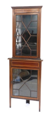 An Edwardian mahogany and satinwood cross banded standing corner cabinet, the top with a moulded cornice, and a single astragal glazed door, the base with a panel and a further astragal glazed door, on tapering legs, 197cm high.