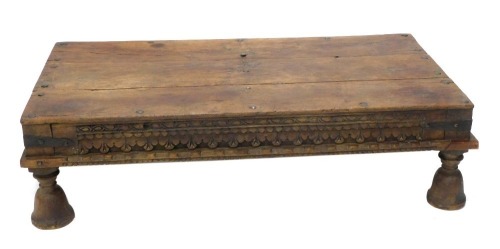 An Eastern hardwood table, the rectangular planked top with iron bolts or nails, above a carved frieze, on bell shaped legs, possibly Indian and constructed from old timber, 40cm high, 51cm wide, 78cm deep.