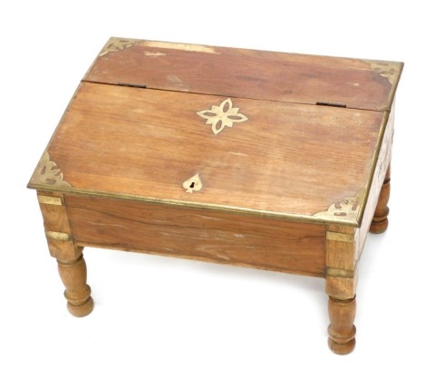 An Eastern hardwood and brass low writing table, the hinged sloped top enclosing a vacant interior, on turned legs, 39cm high, 47cm wide.