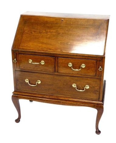 An oak bureau, the fall enclosing a fitted interior above two short and one long drawer with brass drop handles, on cabriole legs, with pad feet, 82cm wide.