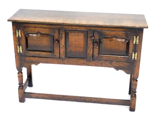 An oak side cabinet, with rectangular top above two panelled doors flanked by a panelled recess, with H hinges, on turned supports, with plain stretchers, 77cm high, 106cm wide.