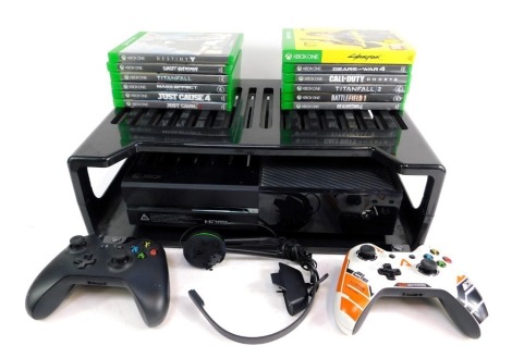 An Xbox one, in black with storage shelf, two controllers and various games to include Cyberpunk, 2077, Titan 42, Call of Duty Ghost, Battlefield 1, Years of War, Just Cause, Destiny and others. (a quantity)