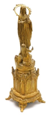 A late 19thC French gilt metal souvenir of Lourdes, showing St Bernadette before the Virgin Mary, beneath title "Miracle du Clerge, Five Aviril 1858", the base of gothic form, cast in relief with churches and gothic windows, raised on four scroll feet, 3