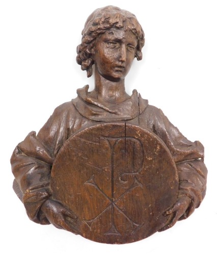 A late 17thC Continental carved wooden bust of a saint, half length, holding a roundel with a sacred monogram, 31cm high.