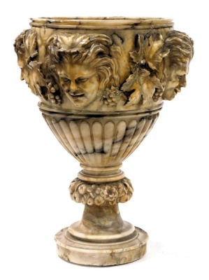 An early 19thC Continental Grand Tour alabaster urn, of semi fluted form, carved with vines and three heads of fauns, raised on a fluted and floral carved and stepped circular socle, 46cm high, 31cm wide.