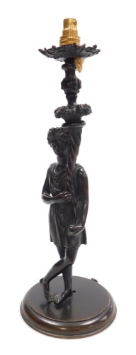 An early 19thC Continental bronze female figure, converted to an electric table lamp, modelled in standing pose, with her legs crossed, holding a cornucopia of fruit, beneath a scrolling stemmed drip tray, raised on a circular wooden base, 38cm high.