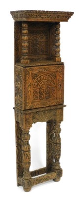 A late 19thC Jacobean style oak cupboard, of narrow proportions, with all over tree and foliate carving, the outswept pediment above a panelled back, raised on turned columns, over a cupboard enclosing a vacant interior, raised on a table base with cup an