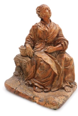 A late 18thC French terracotta figure of a woman, modelled seated with a basket of fruit, raised on a naturalistic base, 17cm wide.