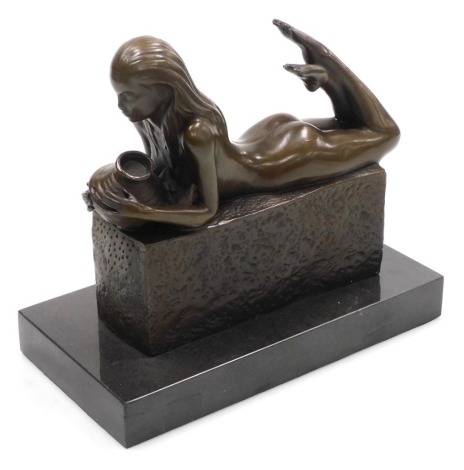 A modern bronze sculpture of a lady, cast naked, lying on her front holding a vase, raised on a rectangular plinth, above a black marble base, 23cm wide.