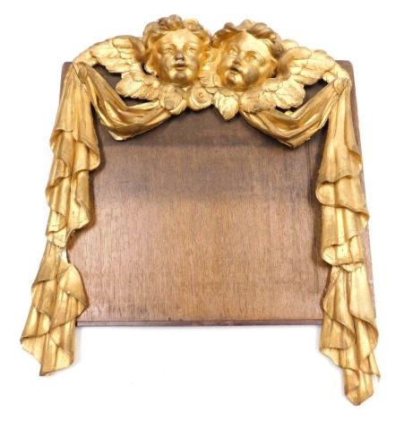 An 18thC gilt wood swag ornamentation, surmounted with a pair cherub's heads, 45cm high, 47cm wide.