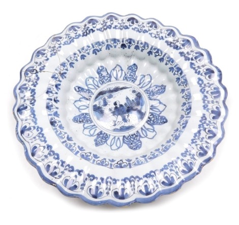 An early 18thC Delft ware blue and white rose water dish, of lobed form, the central roundel depicting a woman seated by a riverbank, within wheat and floral borders, 33cm wide. (AF)