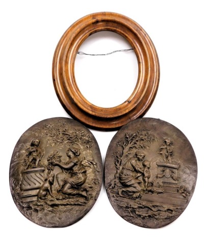 A pair of 19thC bronze cast oval wall plaques, depicting figures and cherubs and trees, one with a wooden frame, 25cm x 19cm.