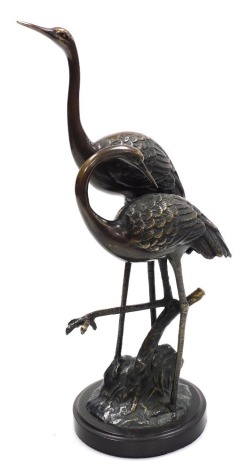 A Japanese Showa period bronze figure group of two storks, each cast in standing pose on a naturalistic ground, raised on a circular base, 36cm high.