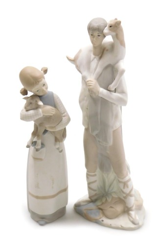 A Lladro bisque porcelain figure of a girl, modelled standing holding a lamb in her arms, 21cm high, and a further figure of a boy, with a goat around his shoulders, 27cm high. (2)