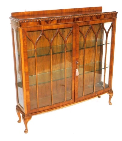 A 1930s walnut bow front display cabinet, with a pair of astragal glazed doors enclosing two glass shelves, raised on cabriole legs, 125cm high, 120cm wide, 31cm deep.