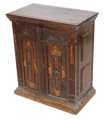 An 18thC Continental oak parquetry cupboard, with two carved panelled doors, enclosing a single shelf, raised on a plinth base, 73cm high, 63cm wide, 37cm deep.