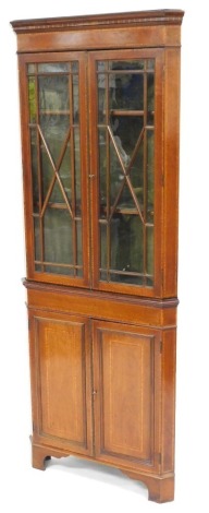 An Edwardian mahogany and satinwood crossbanded corner display cabinet, the pediment over a pair of glazed doors enclosing two shelves, above a pair of cupboard doors, raised on bracket feet, 202cm high, 79cm wide, 43cm deep.