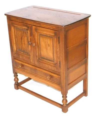 An Ercol elm cupboard, with two doors over one long frieze drawer, raised on turned legs united by a box stretcher, 88cm high, 78.5cm wide, 42cm deep.