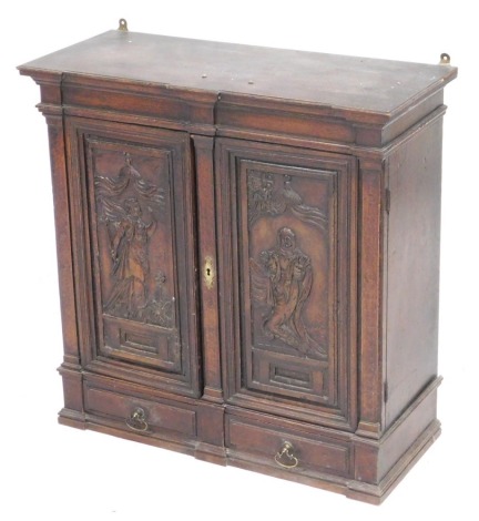 A late 17thC Continental walnut sacristy cabinet, the pediment top over a pair of panelled doors carved with religious figures, opening to reveal a shaped shelf, over two small drawers, 61cm high, 60cm wide, 26cm deep.