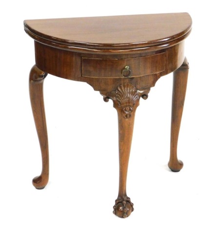 A Georgian style mahogany demi-lune fold over tea table, with a frieze drawer, raised on shell capped cabriole legs, the front leg with a ball and claw foot, 70cm high, 64.5cm wide, 32cm deep.