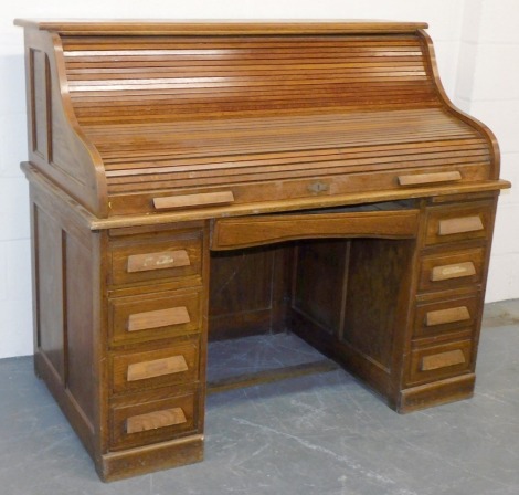 A Victorian oak roll top clerk's desk, with S shaped tambour, enclosing drawers and recesses, above a central drawer flanked by six short and one deep drawer, raised on a plinth base, 123cm high, 137cm wide, 76.5cm deep.