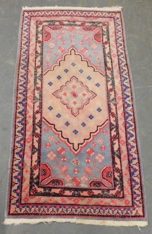 A Baluchi blue and pink ground rug, with a central floral filled medallion, within a floral field and within geometric borders, 180cm x 90cm.