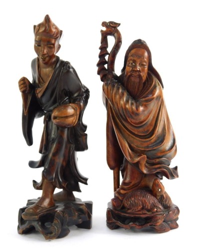 Two Oriental hardwood carvings, depicting an immortal holding staff with animal seated at feet, 24cm high, and a further carving of a youth holding bag, 23cm high.