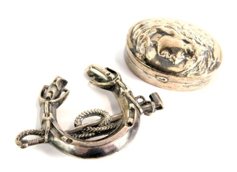 Two silver trinkets, comprising a silver horseshoe and riding whip brooch, 5cm wide, and a white metal pill box, embossed with female head, white metal stamped 925, 3cm diameter, 16.6g all in. (2)