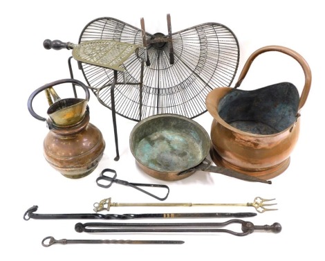 A group of copper and brass wares, comprising a peacock fan fire guard, trivet, ram head poker, copper coal scuttle, saucepan, etc.