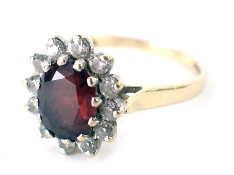 A 9ct gold floral cluster dress ring, the central stone of oval design, in red colouration, surrounded by CZ stones, ring size P½, 3.6g all in.