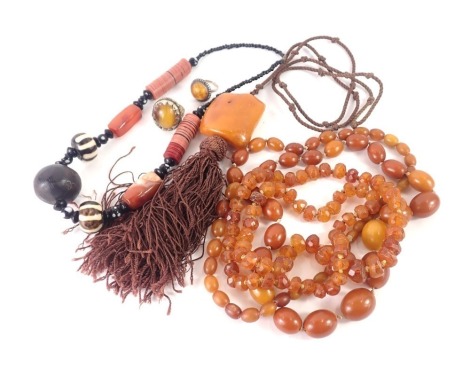 A group of amber and imitation amber jewellery, comprising a butterscotch Baltic amber necklace, on brown string strand, 46.2g, a graduated butterscotch neck chain, the largest bead 2.5cm wide, the smallest 1cm wide, on knotted string strand, 92.7g all in