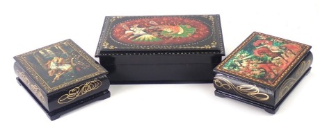 Three Russian black lacquer trinket boxes, decorated with maiden and warrior, figure on horseback, and man and dove, the largest 4cm high, 16cm wide, 10cm deep.