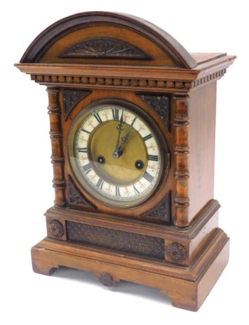 A late 19thC Hamburg Clock Company walnut cased mantel clock, circular brass dial with enamel chapter ring bearing Roman numerals, fourteen day strike movement, the case of architectural form, with a domed pediment, the case with carved spandrels and turn