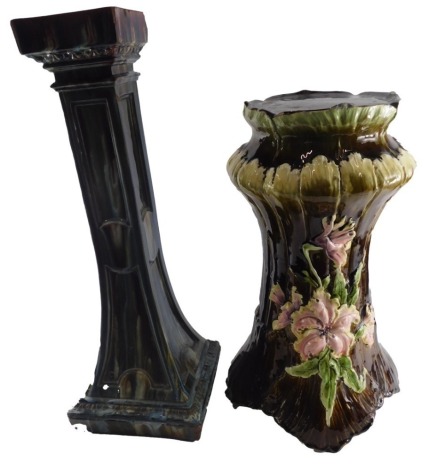 A 19thC Continental Majolica coloured ceramic pedestal, with raised decoration of flowers, leaves, etc., on a brown ground, numbers to underside, 56cm high, and another. (AF)