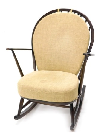 An Ercol rocking chair, with gold upholstery. The upholstery in this lot does not comply with the 1988 (Fire & Fire Furnishing) Regulations, unless sold to a known exporter or upholsterer it will be cut from the frame before leaving the premises.