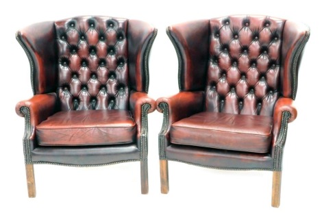 A pair of ox blood red buttoned back wing armchairs, with studded finish.