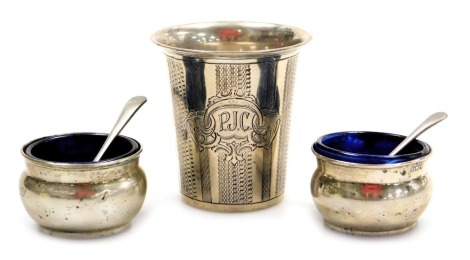 A late 19thC Continental beaker, white metal, with engine turned banding, shield reserve, monogram engraved, white metal, 1.68oz, together with a pair of Edward VII silver circular salts, with blue glass liners, and plated spoons, London 1905, 0.9oz. (3)