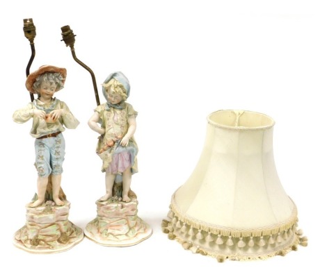 A pair of late 19thC Continental figural table lamps, modelled as boy and girl urchins with pomegranates, raised on naturalistic grounds, with shades, 60cm high.