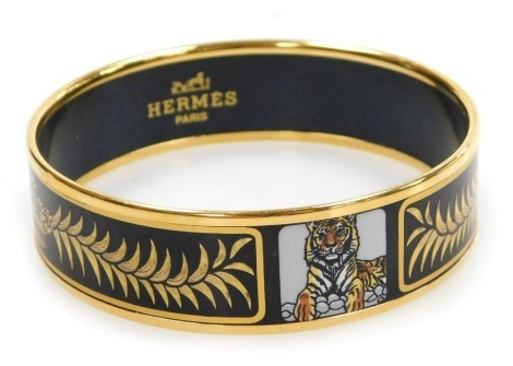 An Hermes gold plated and enamel bangle, decorated with tigers, crowns and wreaths, on a black ground, 6.5cm wide.