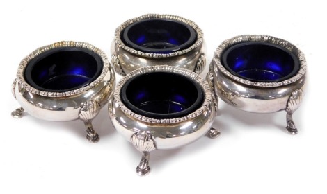 A set of four Edwardian silver circular salts, raised on three leaf capped paw feet, with blue glass liners, Chester 1910, 6.55oz.