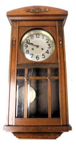 An early 20thC mahogany cased wall clock, the silvered dial bearing Arabic numerals, eight day movement with coil strike, the case with foliate carving and bevelled glass inset door, with pendulum and key, 72cm high.