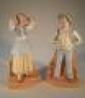 A pair of 20thC bisque figures of a young man and a young girl standing by a wall (AF)