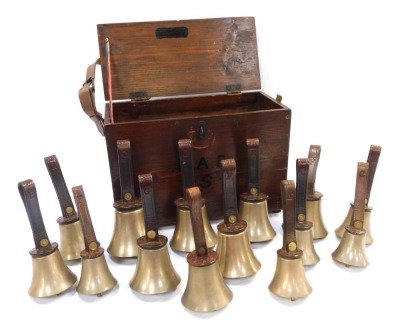 Fourteen brass hand bells by Warners of London, comprising G (2), F (2), E (2), D (2), C (2), A, F II and A II, each with a leather strap embossed with Warners of London, contained in a stained pine case with leather handle, (handle AF).