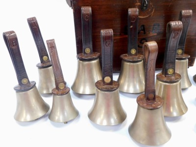 Fourteen brass hand bells by Warners of London, comprising G (2), F (2), E (2), D (2), C (2), A, F II and A II, each with a leather strap embossed with Warners of London, contained in a stained pine case with leather handle, (handle AF). - 2