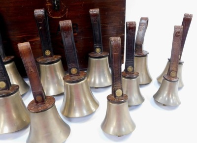 Fourteen brass hand bells by Warners of London, comprising G (2), F (2), E (2), D (2), C (2), A, F II and A II, each with a leather strap embossed with Warners of London, contained in a stained pine case with leather handle, (handle AF). - 3