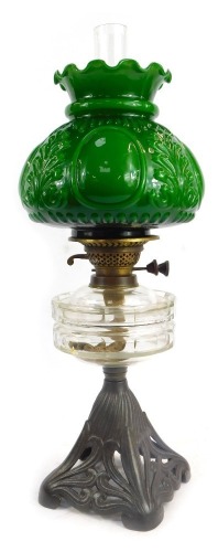 A 19thC oil lamp, with green moulded glass shade, clear glass central reservoir, on a cast pierced metal base, decorated with scrolls, with chimney, 60cm high overall.