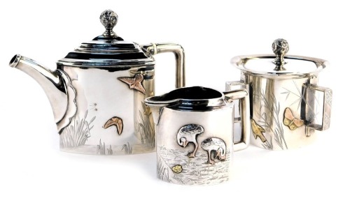 A Victorian Aesthetic influence silver three piece tea service, comprising teapot, lidded three handled sugar bowl and milk jug, each piece of curved triangular form, relief decorated with birds, gilt heightened birds, bright cut decoration of reeds, wate