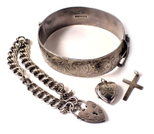 A group of silver jewellery, comprising a silver half hinged bangle with floral scroll decoration and safety chain, 6.5cm diameter, a silver crucifix pendant heart shaped locket and a fancy link bracelet with heart shaped padlock, 74.8g all in. (4)