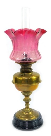 A 19thC brass oil lamp, with floral etched cranberry shade, brass reservoir, on turned column, on black stepped glass base, with chimney, 60cm high overall.