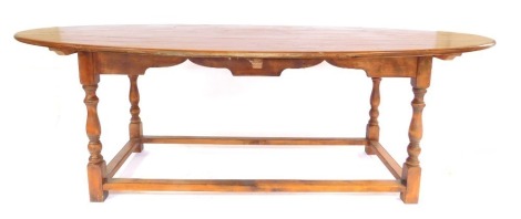 A large fruitwood oval kitchen table, the plank top, shaped apron on turned supports with stretchers, 78cm high, the top 266cm x 151cm.